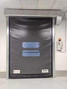 Nell'immagine si vede, in primo piano, una porta rapida autoriparante con il telo di color nero, munito di doppia finestratura trasparente, per la compartimentazione dei reparti. Il color nero è coordinato con i colori aziendali. 