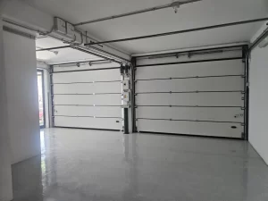 Nell'immagine si vede in primo piano una coppia di portoni sezionali chiusi, installati per la chiusura esterna.
