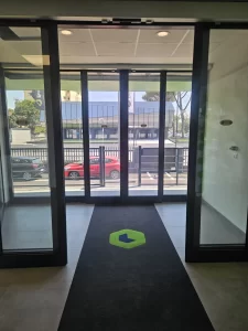 Nell'immagine si vede la bussola dell'ingresso pedonale con gestita con due porte automatiche scorrevoli con ciascuna due ante mobili e due fisse, automazione ridondante valida come uscita di sicurezza. nell'immagine le ante della porta esterna sono in posizione di chiusura mentre quelle della porta automatica interna sono aperte nella massima posizione. 