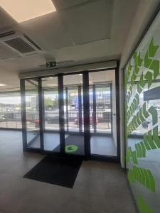 Nell'immagine si vede la bussola dell'ingresso pedonale con gestita con due porte automatiche scorrevoli con ciascuna due ante mobili e due fisse, automazione ridondante valida come uscita di sicurezza.