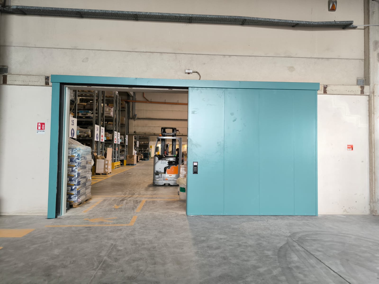 Nell'immagine si vede un portone scorrevole tagliafuoco di colore azzurro che separa il magazzino dall'area produttiva di un'azienda manifatturiera.
