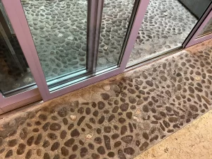 Bussola con porta automatica all’ingresso di Palazzo Trentini. Dettaglio della guida incassata nella pavimentazione in ciottolato storico.