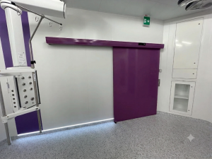 In questa foto si vede l'ingresso di una sala operatoria gestito attraverso una porta automatica scorrevole ad un anta con tenuta ermetica. Il pavimento è grigio, i muri sono bianchi mentre l'anta della porta ed il cassonetto dove trovano posto il quadro comando ed i meccanismi di movimento è di un gradevole color viola. 