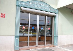 L'immagine mostra una elegante porta automatica con due ante fisse e due mobili installata in un prestigioso storico panificio siciliano. la porta automatica è inserita all'inerno di una cornide con elegante arco decorativo