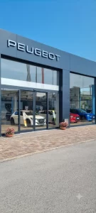 Nell'immagine si vede l'edificio della più importante concessionaria Peugeot. All'ingresso una porta automatica scorrevole con due ante fisse e due mobili.