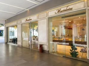 In questa foto un elegante bar pasticceria situato sotto i portici. Due distinte porte automatiche scorrevoli ad un anta in cristallo gestiscono ingressi ed uscite. Attraverso le ampie vetrate si vedono banchi colmi di squisite paste siciliane.