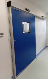 Porta scorrevole a chiusura ermetica installata all'ingresso di sala operatoria. Pannello blu con inserita visiva trasparente complanare. Cassonetto con motorizzazione e rada di attivazione apertura e chiusura automatica.