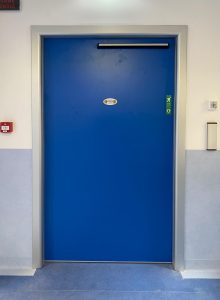 porte automatica a battente di colore blu installata all'uscita di un locale tecnico nell'area delle sale operatorie