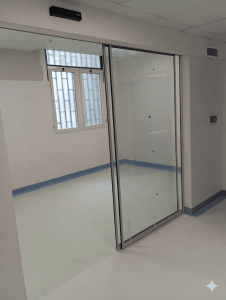 Nell'immagine: porta automatica scorrevole per locale visite mediche. Con un'anta mobile ed un'anta fissa entrambe tutto vetro. Serramento sottile, vetro infrangibile a norma. Sulla parete si vede il radar di attivazione apertura e chiusura.