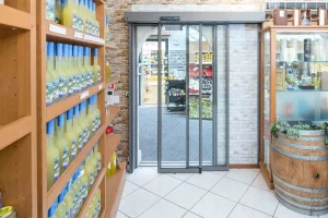 Nell'immagine si vede l'ingresso di un piccolo negozio di città. Lo spazio di passaggio è stretto e pertanto è stata installata una porta automatica scorrevole con 3 ante telescopiche di cui due mobili ed una fissa.