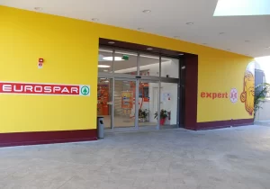 L'ingresso di questo supermercato EUROSPAR è gestita con un'ampia porta automatica scorrevole dotata di due ante fisse e due ante mobili a sfondamento integrale.