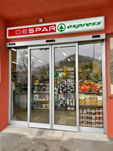 In questa immagine si vede l'ingresso di un supermercato Despar express di città. Il piccolo ingresso è gestito da una porta automatica con due ante mobili a sfondamento e due ante fisse.