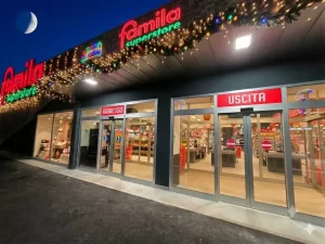 Nella foto scattata in notturna si vedono gli ingressi e le uscite di un ipermercato Famila. Ingressi ed uscite sono gestiti da porte automatiche scorrevoli rettilinee con ciascuna due ante mobili a sfondamento per vie di fuga.