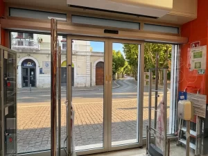 In questa foto si vede l'uscita di un supermercato realizzata con una porta automatica scorrevole con due ante fisse e due ante mobili a sfondamento parziale. Sopra la porta si vede l'apparato della lama d'aria installato per gestire gli sbalzi termici con l'esterno.