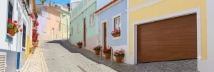 Nell'immagine si vede una stretta strada in salita di un paese caratteristico. Ai lati della strada si vede un continuo di casette colorate. Nella facciata della prima casetta si apre un garage chiuso da una porta sezionale color noce. L'ingresso si trova su una porzione di strada particolarmente inclinata. Per questo motivo l'ultimo pannello inferiore della porte del garage non ha la classica forma rettangolare, bensì a trapezio, per seguire in modo complanare l'inclinazione della strada.