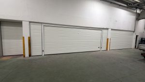 due portoni sezionali chiusi realizzati con eleganti pannelli bianchi con finitura liscia e doga media. A lato i tamponamenti sulle pareti nelle medesime finiture.