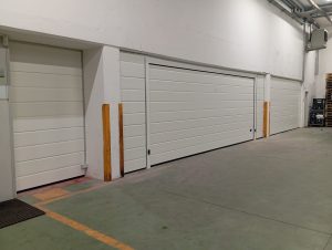 due portoni sezionali chiusi realizzati con eleganti pannelli bianchi con finitura liscia e doga media. A lato i tamponamenti sulle pareti nelle medesime finiture.