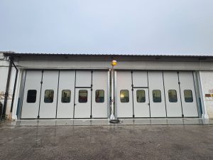 portone industriale a libro con ante ripiegabili laterali: 5 pannelli a sinistra e 5 a destra che chiudono l'intero ingresso, per un totale di 12 metri di larghezza