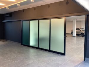 Una parete mobile scorrevole automatica con vetrate in cristallo infrangibile satinato, divide la sala esposizione dal reparti di consegna delle autovetture.