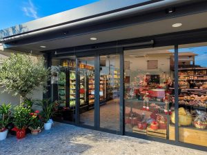 Nell'immagine si vede un negozio di alimentari di paese con ampie vetrate e una porta automatica scorrevole con due ante mobili e sistema ridondante per vie di fuga.
