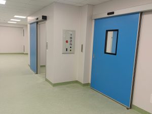 nell'immagine si vedono due porte automatiche per ambiente ospedaliero di colore blu di sui una corredata con visiva trasparente e tenuta ermetica, che danno accesso ai reparti di sale operatorie e reparti ad atmosfera controllata. 